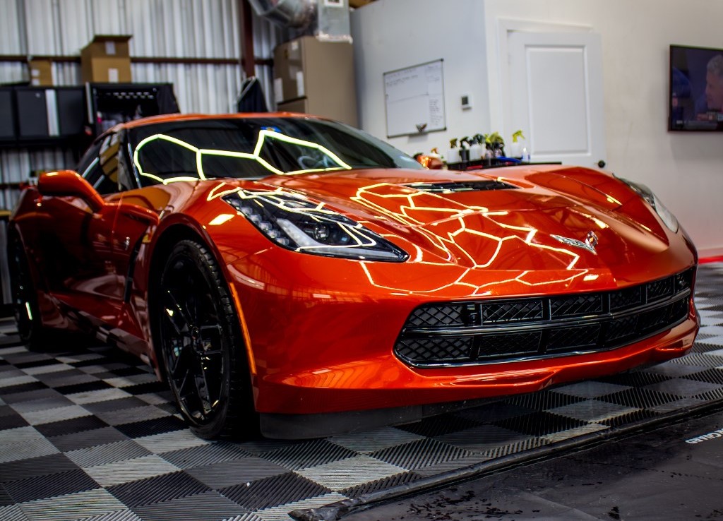 Shiny orange corvette in a professional detailing shop, showcasing the high-gloss finish achieved through ceramic coating.