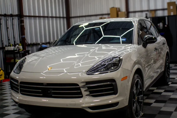 White Porsche SUV under hexagonal lights in a professional detailing shop, highlighting meticulous ceramic coating services at Fort Worth Auto Detail